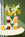 The Giza Paper Vase by OCTAEVO with yellow and white flowers sits on a round table near a pear, green wall behind.