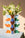 The Giza Paper Vase by OCTAEVO holds white and yellow flowers on a light blue table with a beige background.