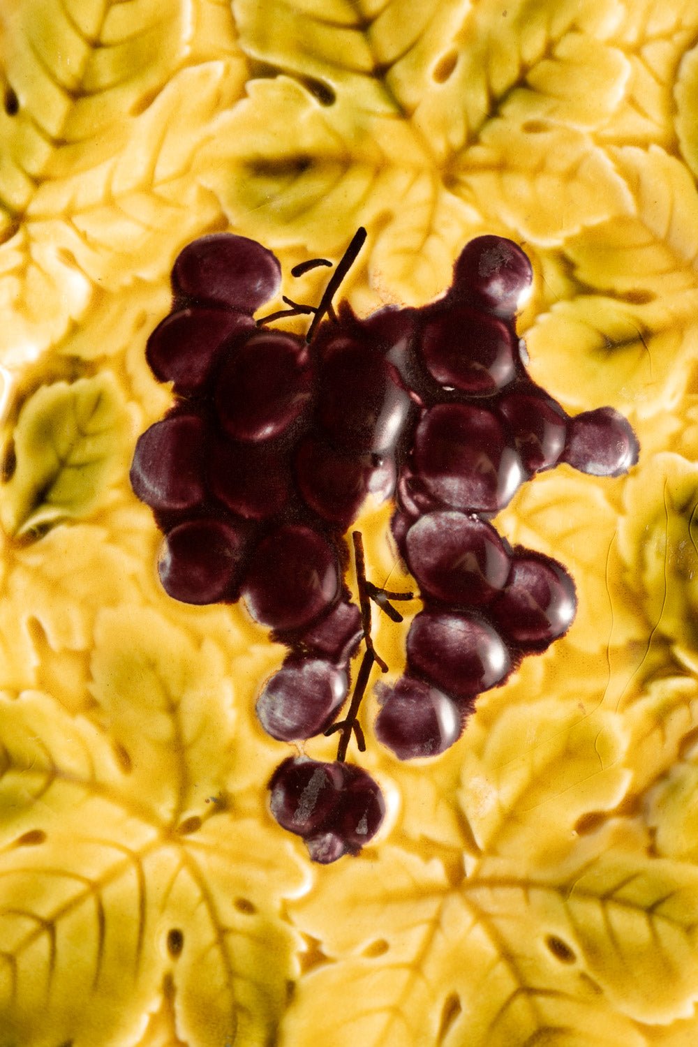 A cluster of dark grapes rests on the OCTAEVO Grape Majolica Plate, embossed with an Art Nouveau leaf pattern.