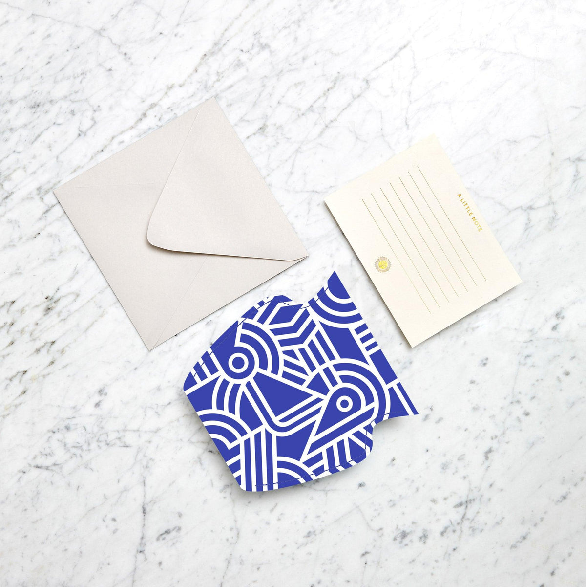 Flat lay of a blank envelope, notecard, abstract card, and Octaevos Greco Mini Paper Vase on a marble surface.
