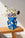 The Blue Hamsa Mini Paper Vase by OCTAEVO features colorful hand designs and holds flowers on a sunlit wooden table.