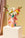 A pink OCTAEVO paper vase decorated with colorful hand illustrations, filled with flowers, displayed on a pedestal.