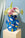 The Hamsa Paper Vase by OCTAEVO, with colorful hand patterns, holds assorted flowers on a light blue background.