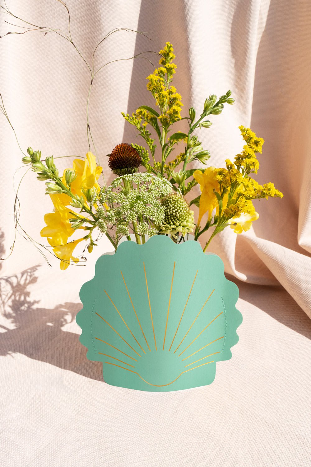 A bouquet of yellow and green flowers in the OCTAEVO Hera Mini Paper Vase against a light fabric background.