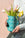 A person holds the OCTAEVO Icarus Mini Paper Vase with tulips and daffodils against a light pink background.