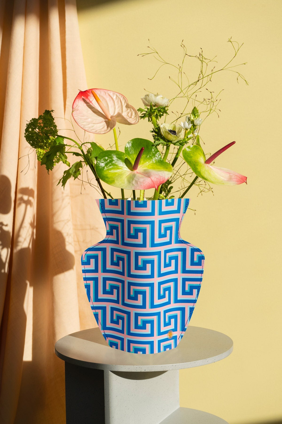 The OCTAEVO Icarus Paper Vase with assorted flowers sits on a small table, bathed in sunlight.