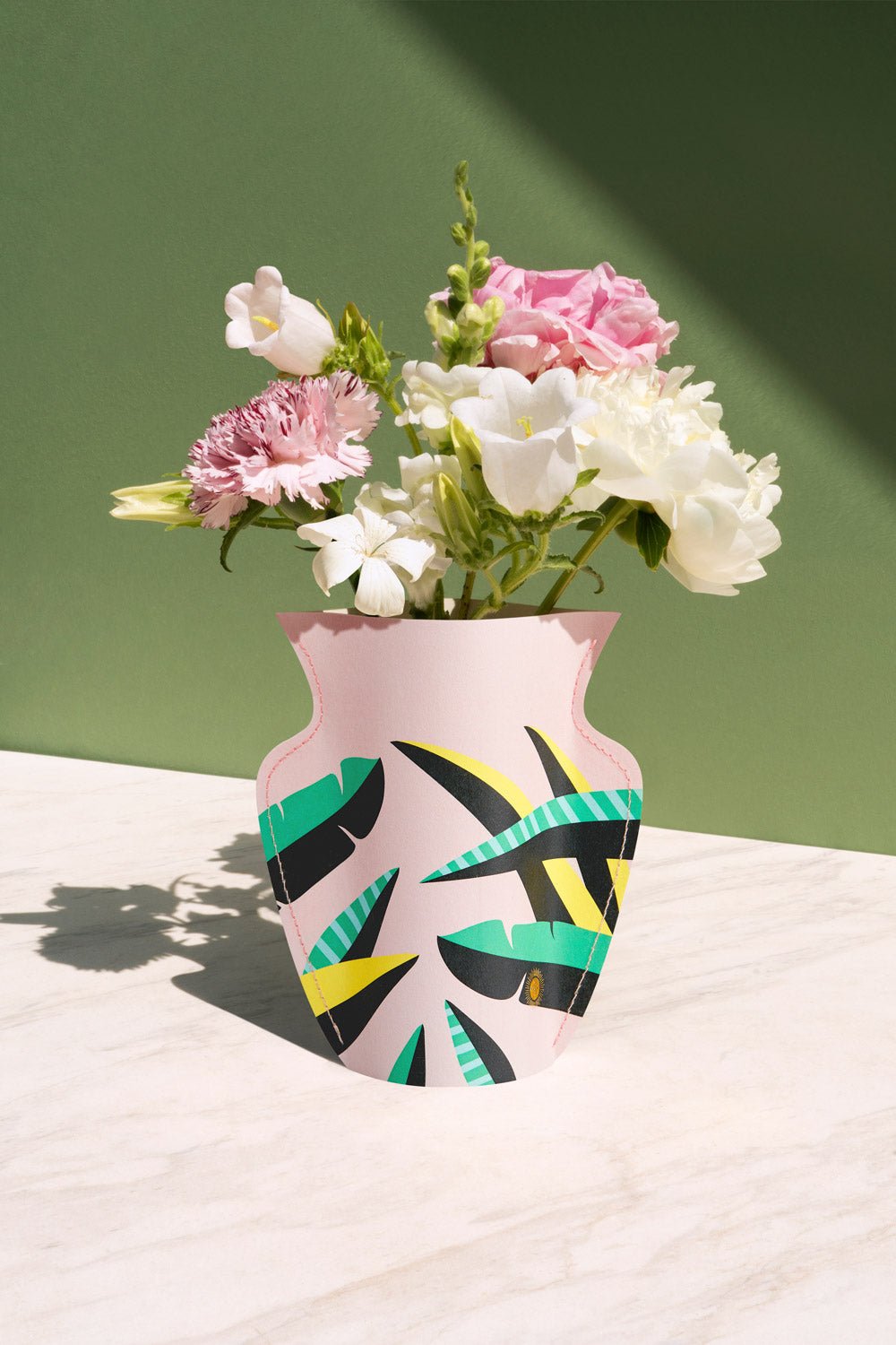 A vibrant bouquet in the OCTAEVO Le Club Mini Paper Vase sits on a white surface with a green background.