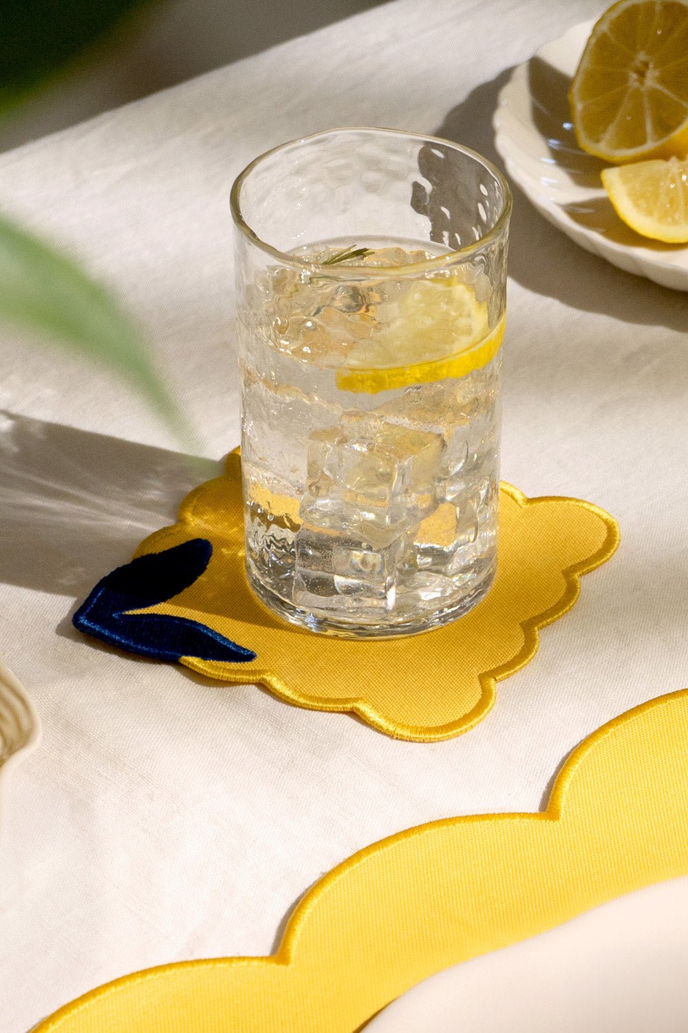 Ein Glas Wasser mit Eis und Zitrone steht auf einem OCTAEVO Untersetzer Zitrone auf einer weißen Tischdecke.
