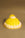 The Mimosa Cake Candle by Octaevo is a yellow and white frosted dessert-shaped candle on a gold base.