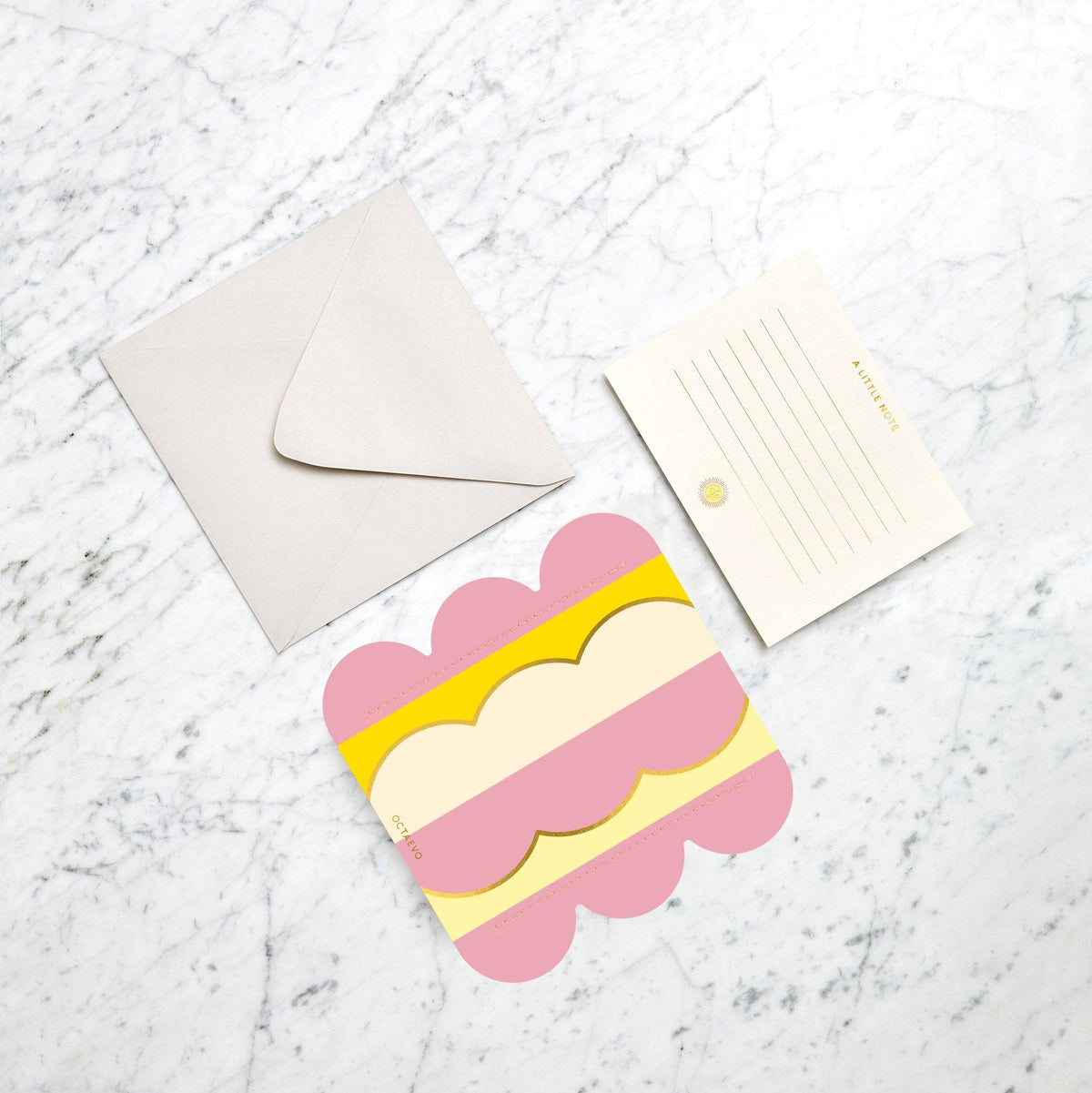 Un mini vase en papier Riviera Wave par OCTAEVO posé à côté d'une carte vierge et d'une enveloppe, dans une ambiance méditerranéenne.