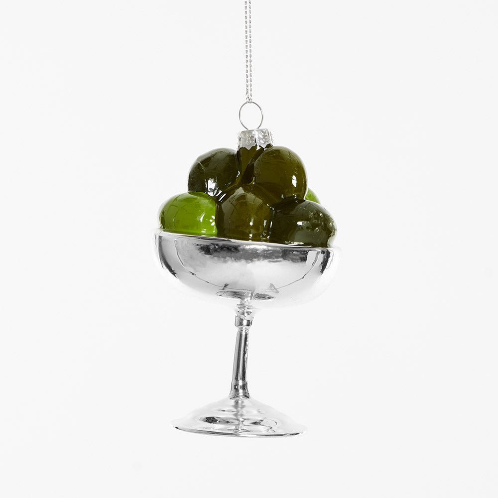 The OCTAEVO Olive Coupe Ornament is a shiny silver holiday decoration shaped like a glass filled with green olives.