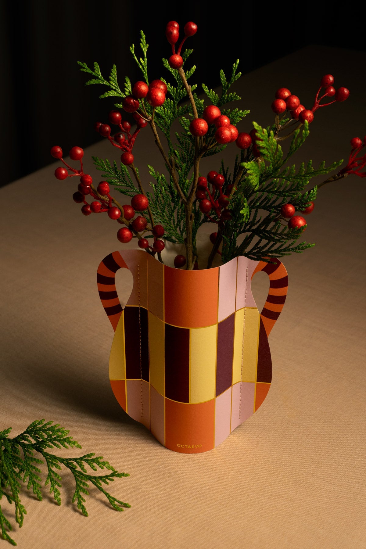 Die OCTAEVO Patio Mini-Papiervase präsentiert grünes Laub und rote Beeren auf einem beigen Tisch, daneben weiteres Grün.