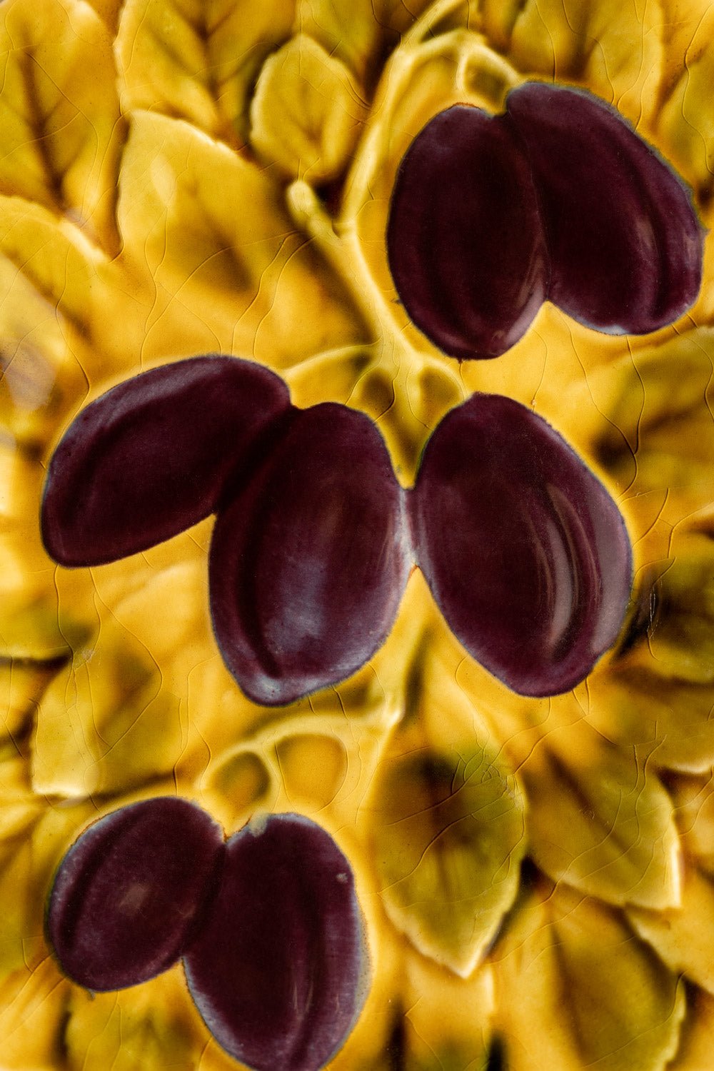 Four dark purple plums with yellow-green leaves grace the OCTAEVO Plum Majolica Plate, evoking French elegance.