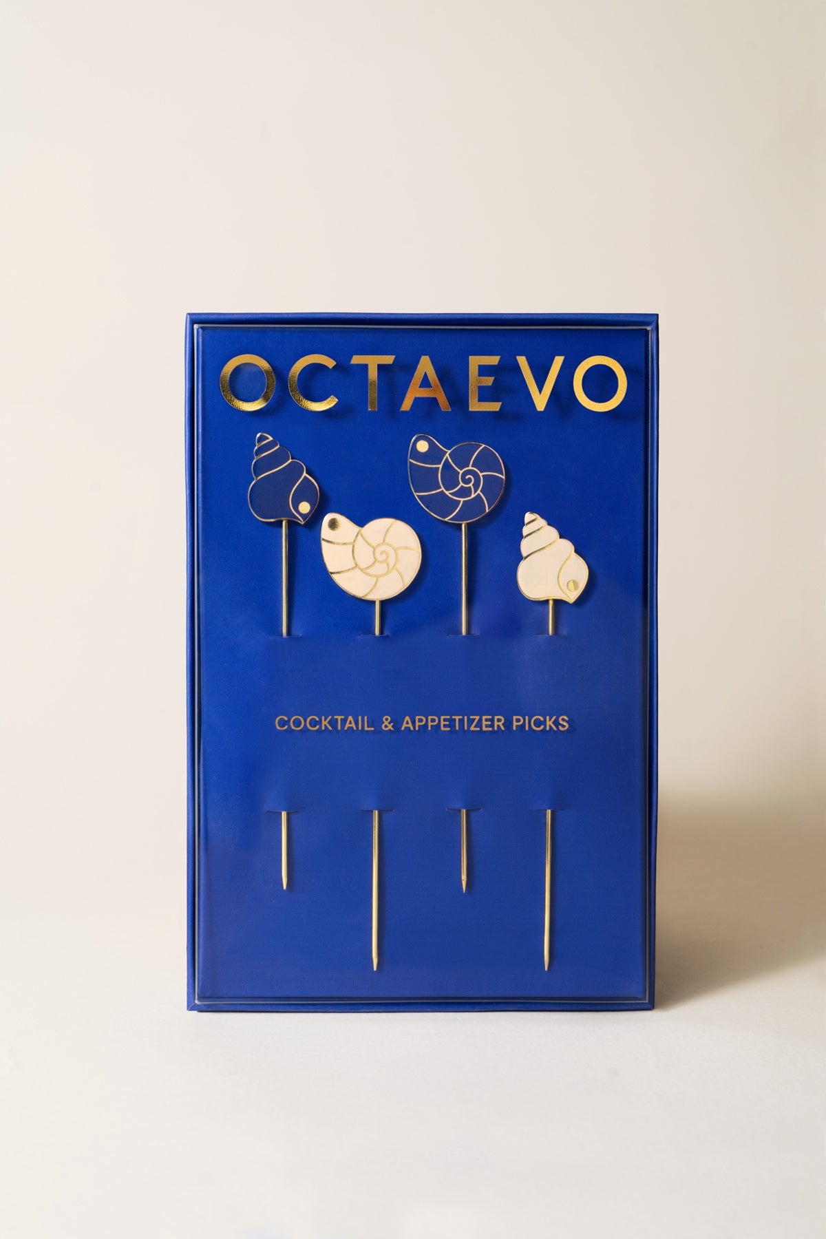 A blue OCTAEVO box holds four gold-plated cocktail picks, each topped with a chic pearl shell motif.