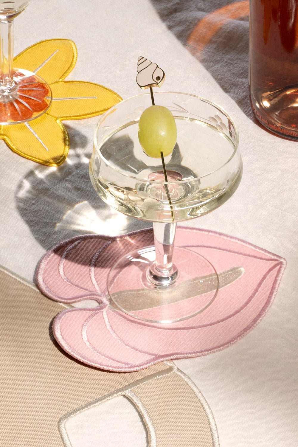 Ein Cocktailglas mit einer grünen Weintraube als Garnitur steht auf OCTAEVO Untersetzern Anthurie in Rosa auf einer bunten Tischdecke.