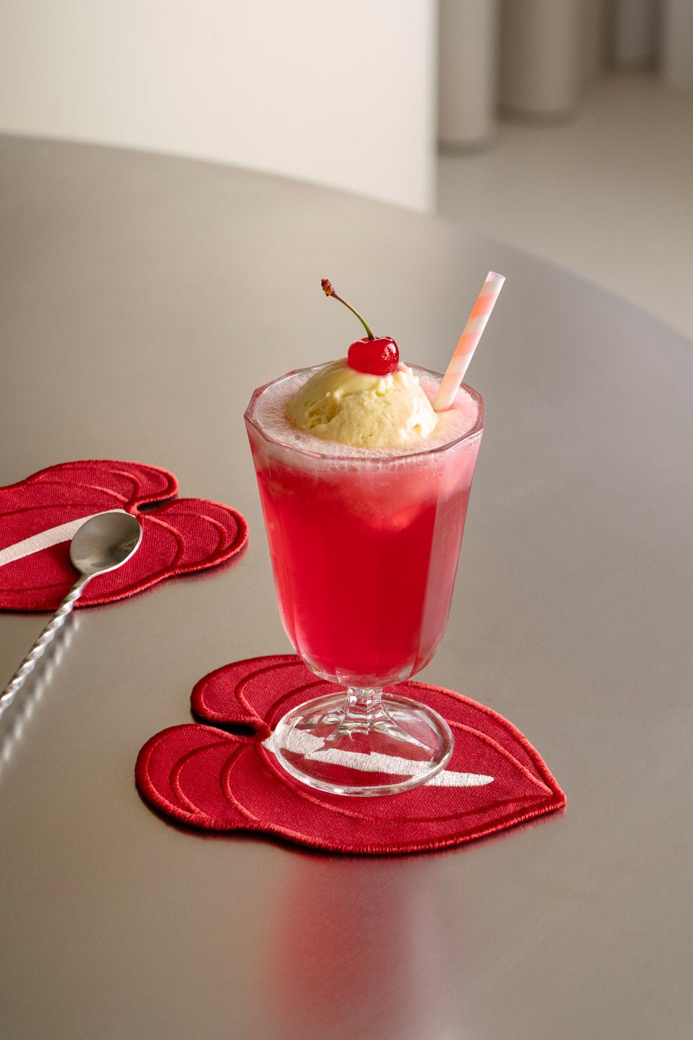 A pink float with ice cream and cherry sits on an Octaevo Red Anthurium Coaster, spoon beside it.