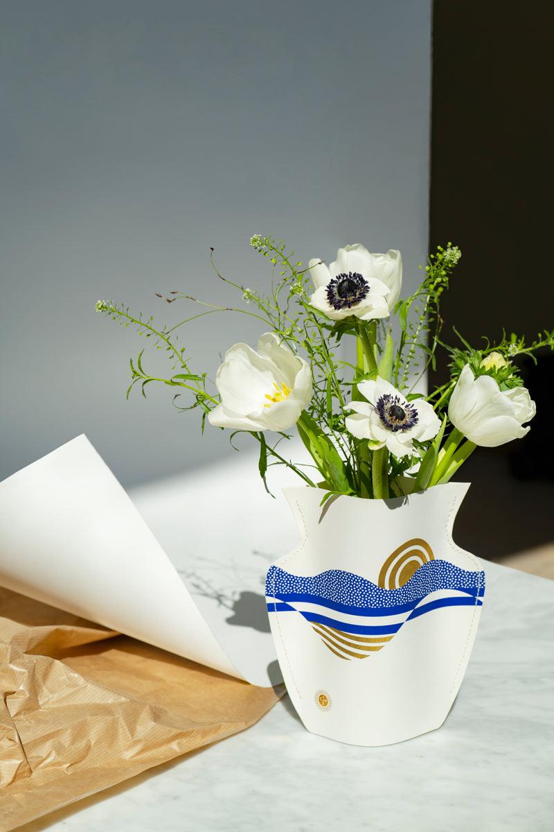 White and purple flowers in the Salina Mini Paper Vase by Octaevo on marble, with wrapping paper unrolled beside them.