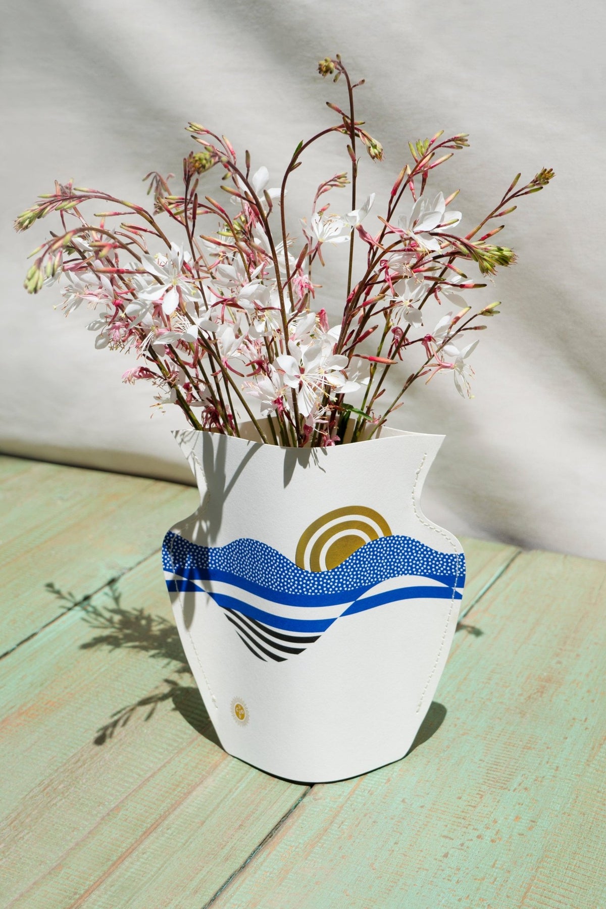 The Salina Mini Paper Vase by Octaevo features a blue and gold abstract design, displayed on a light green surface.