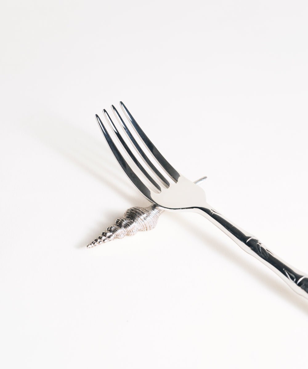 Silver fork on sea shell knife rest on a white background