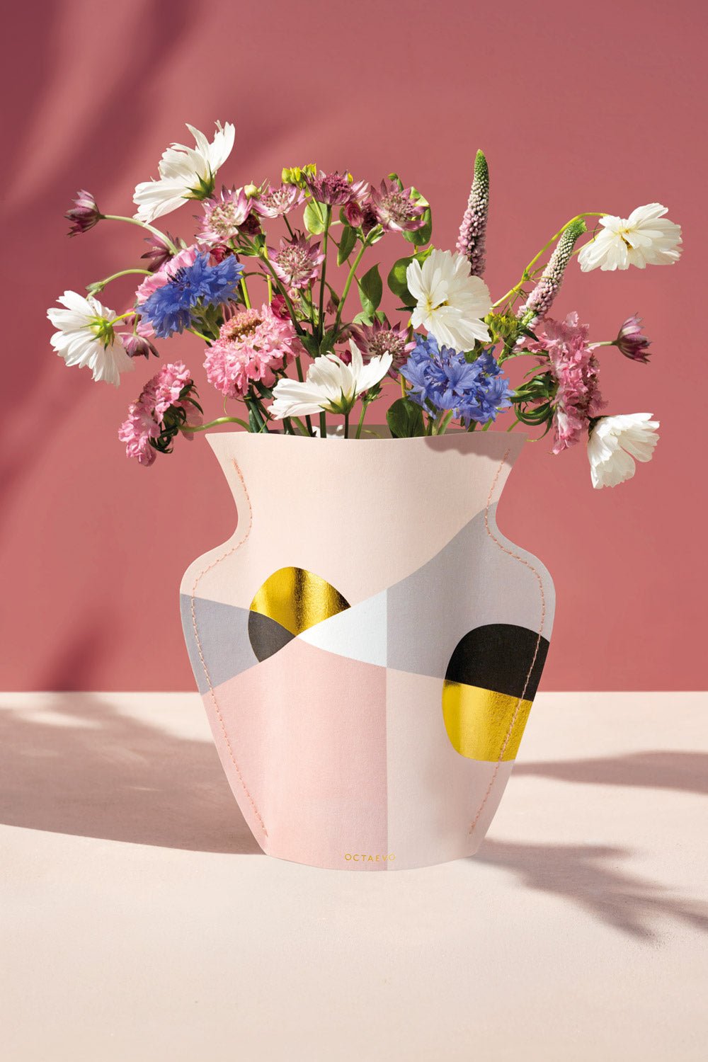 The OCTAEVO Siena Mini Paper Vase with geometric patterns holds wildflowers against a pink background.