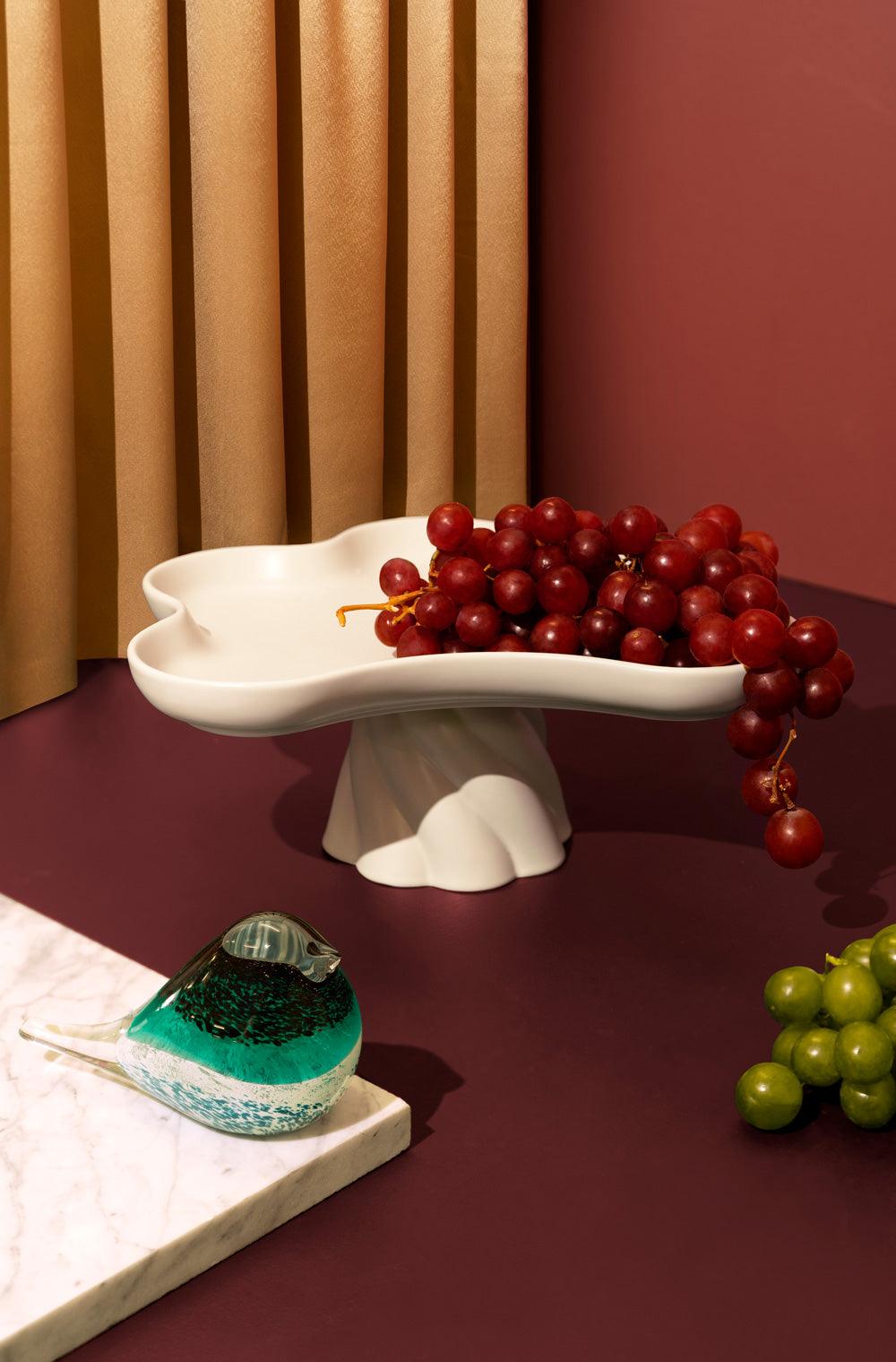 Red grapes on Octaevo’s ivory, flower-shaped Templo High Tray make a striking centerpiece with glass and green grapes.