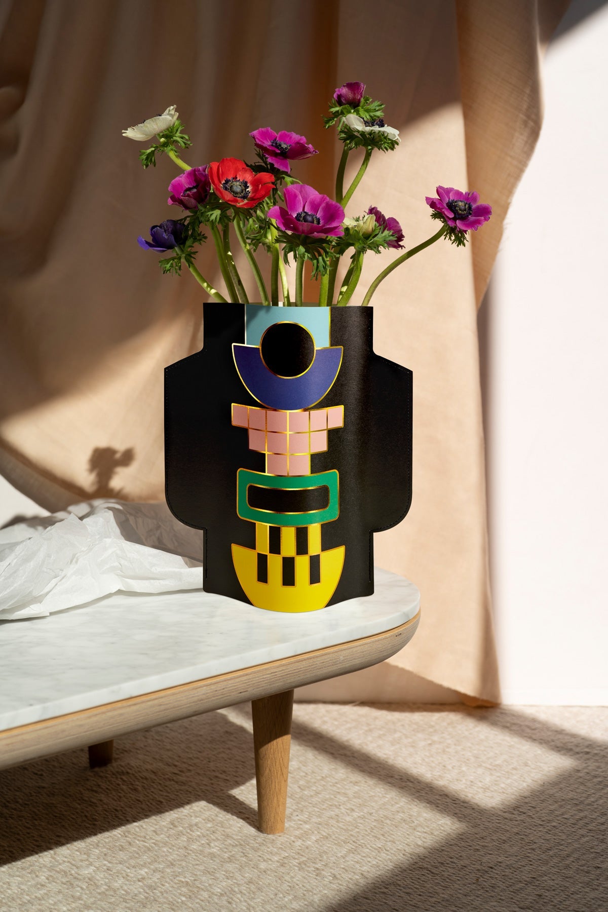 The OCTAEVO Templo Paper Vase in black brightens a marble table with Mediterranean flair and vibrant blooms in sunlight.