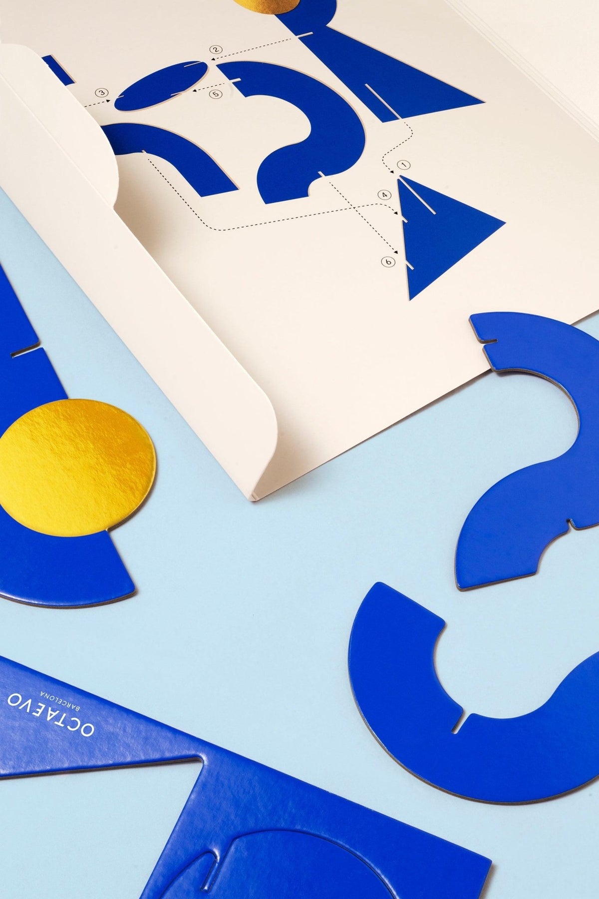 Octaevos Water Paper Sculpture features blue and yellow geometric decor on a light blue surface with an open envelope.