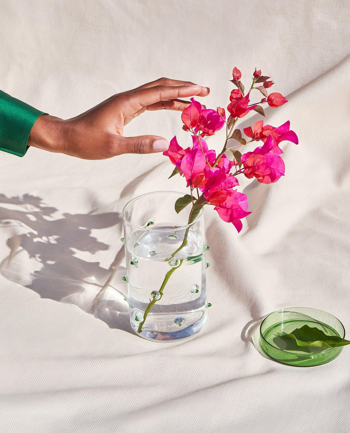Eine Hand greift nach dem OCTAEVO Agave Glasbehälter Groß neben rosa Blumen vor einem hellen Stoffhintergrund.