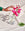 A hand reaches for the OCTAEVO Agave Glass Container Large beside pink flowers on a light fabric background.