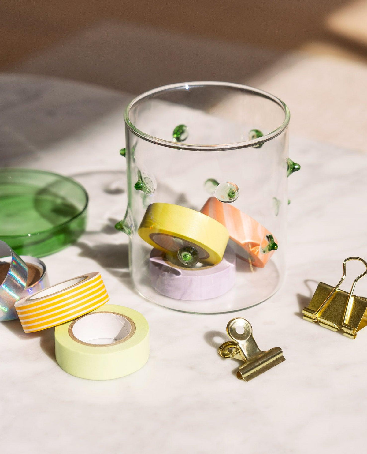 Le contenant en verre Agave Petit format par OCTAEVO range des rubans washi et des clips, sur une table en marbre.