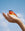 A hand gently holds an orange OCTAEVO Atlas Glass Bird, a vibrant statement piece, against a blue sky.