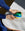 Someone in a blue sleeve holds the blue OCTAEVO Atlas Glass Bird, a vibrant decor piece, on a marble table.
