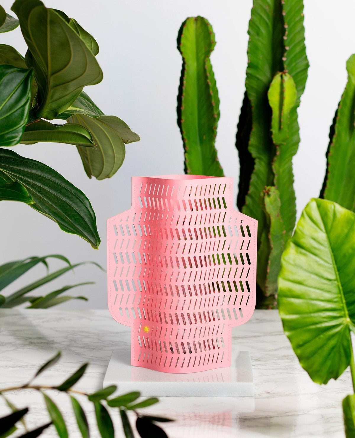 Le vase en papier Aurea par OCTAEVO, une pièce rose faite à la main aux motifs découpés, est présenté parmi des plantes vertes.
