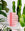 The Aurea Paper Vase by OCTAEVO, a pink handcrafted piece with cut-out patterns, is displayed among green plants.