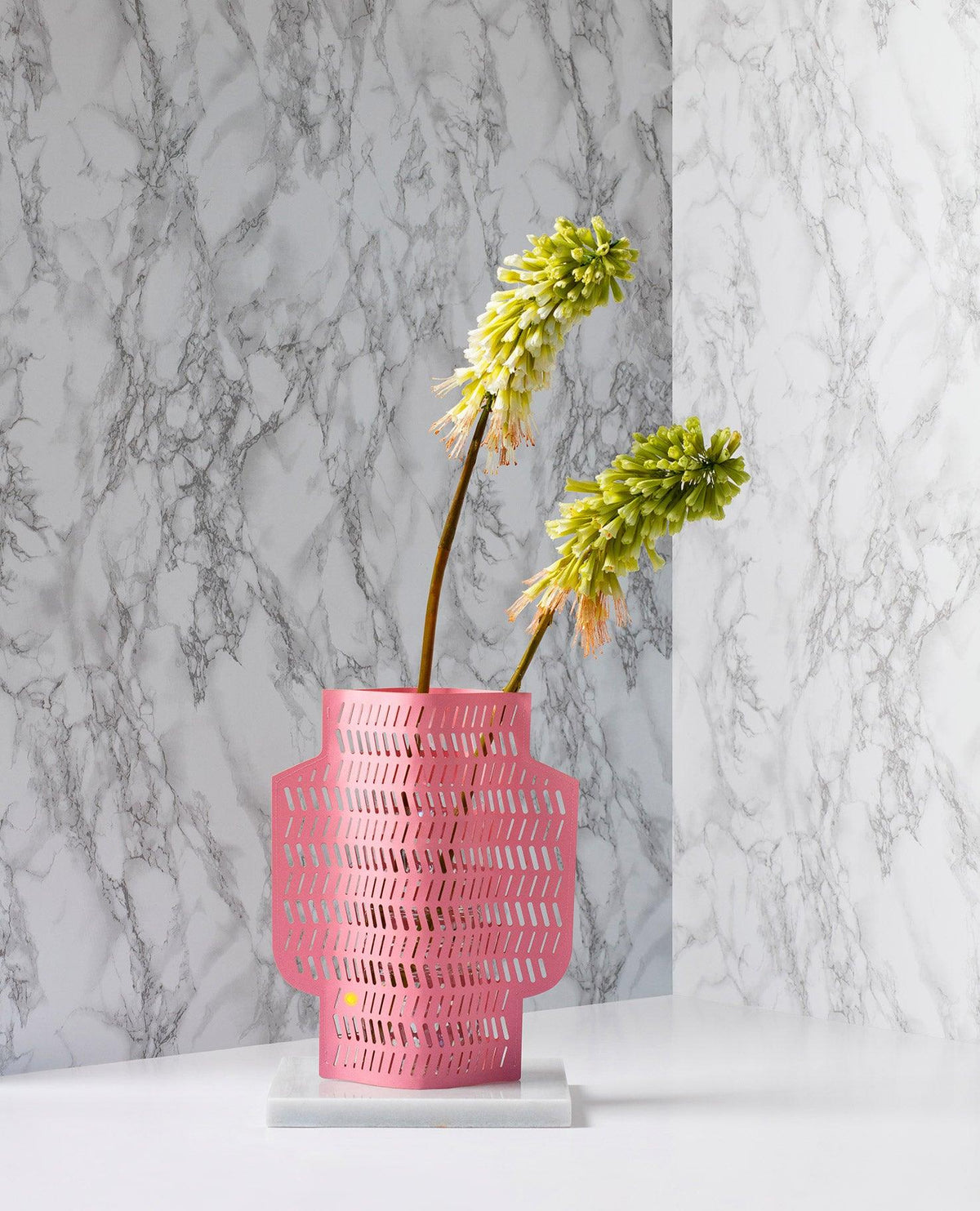Deux fleurs jaune-vert dans le vase en papier Aurea fait à la main par OCTAEVO, devant un fond blanc à motif de marbre.