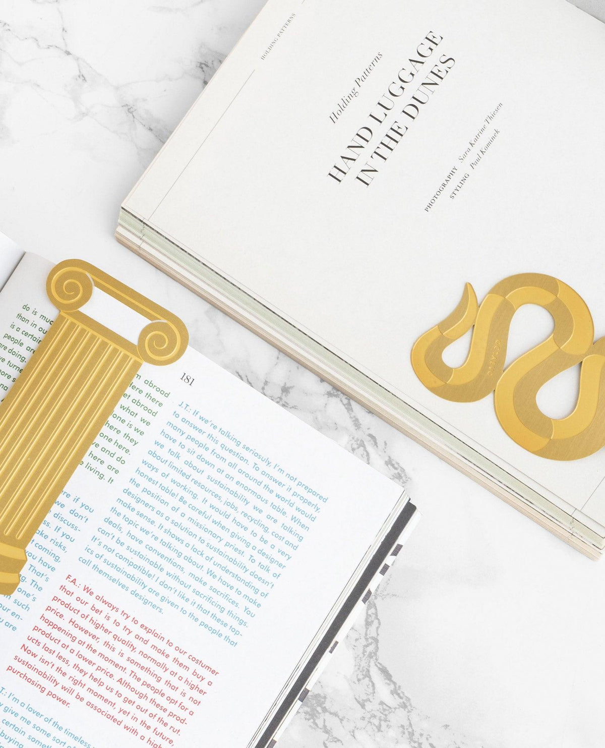 Open books with OCTAEVOs brass Bookmark Artemis and Serpenti, inspired by the Greek Temple, on marble.