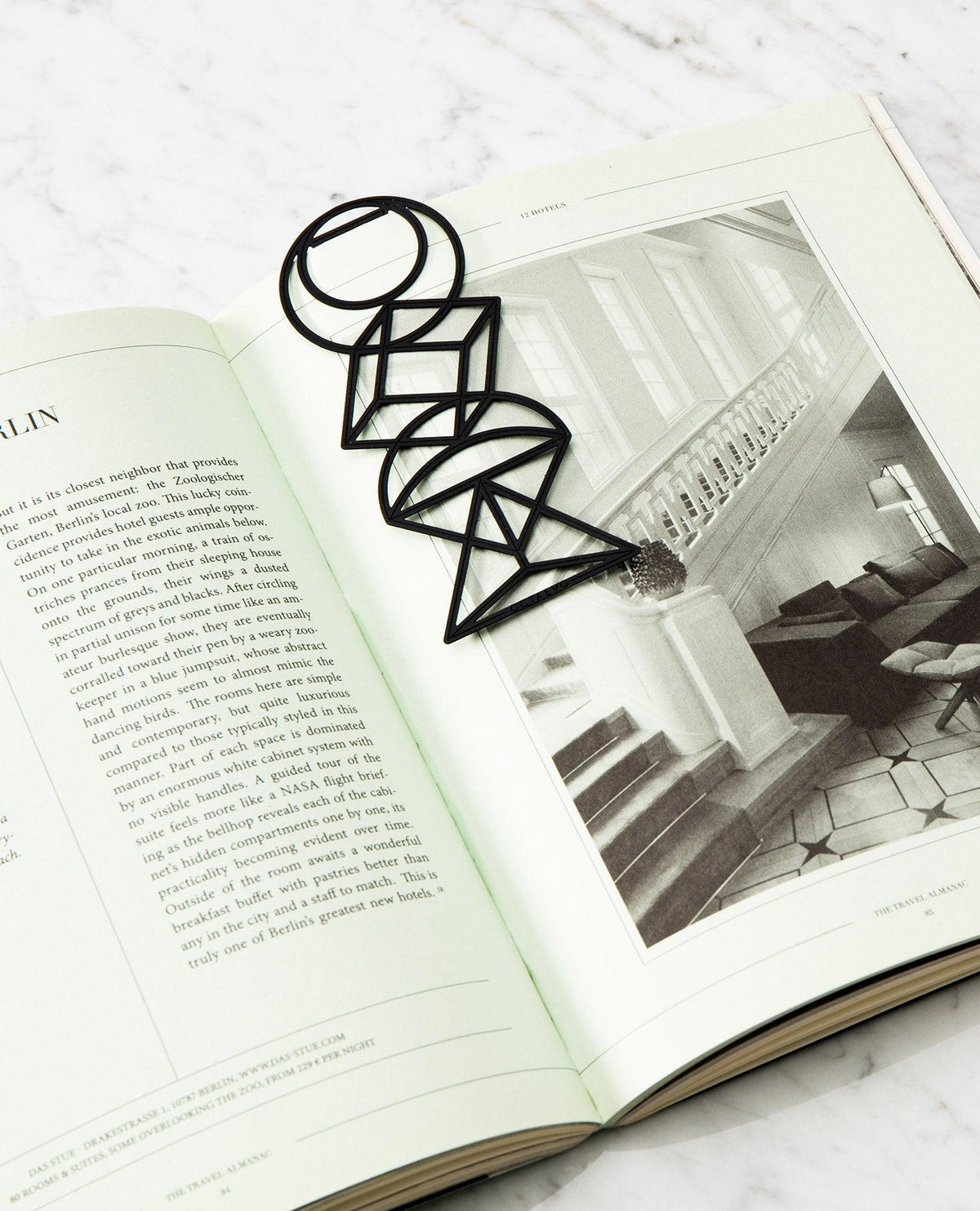 Bookmark Euclid by OCTAEVO, a finely-cut geometric black brass piece, rests on an open book. 