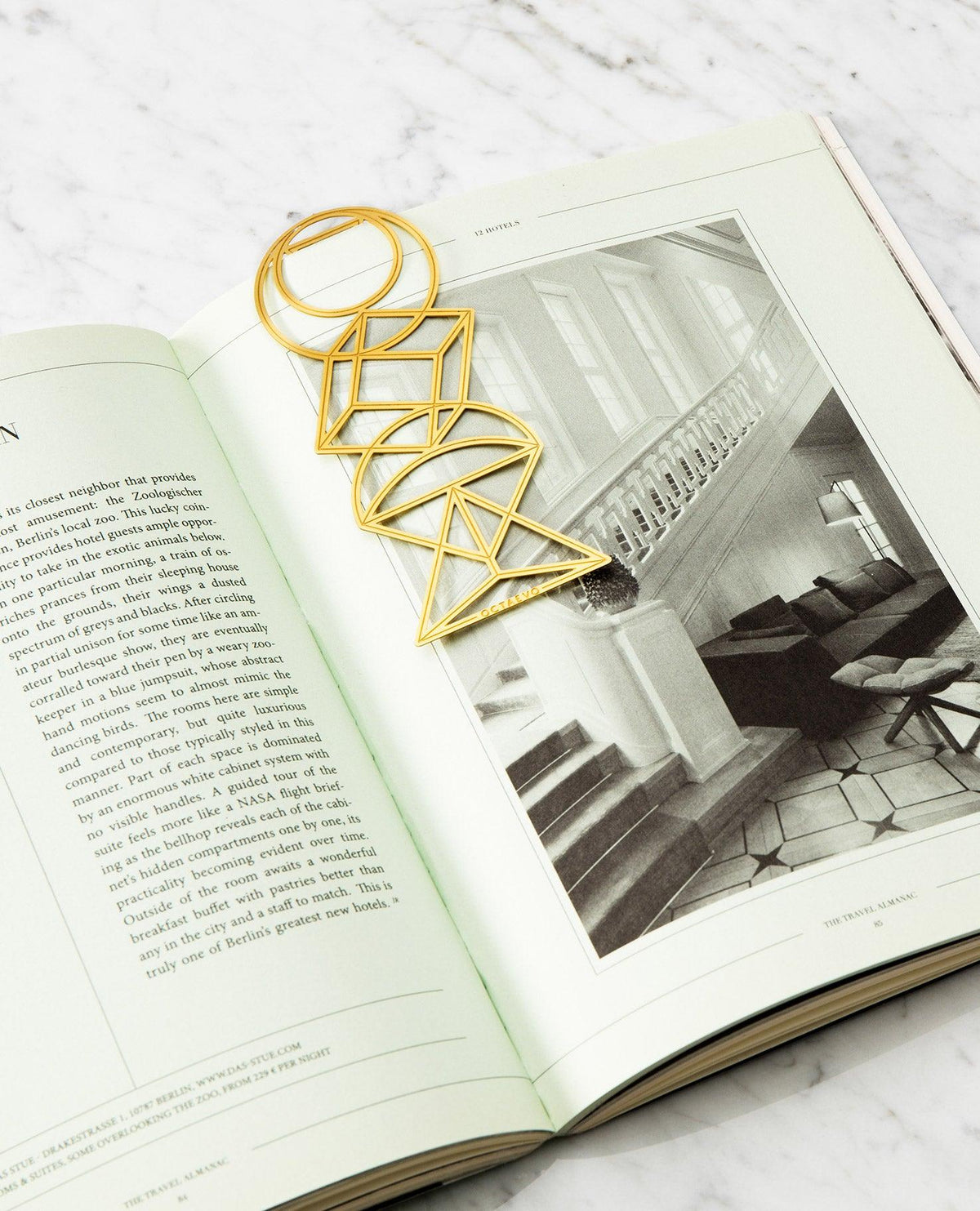 The OCTAEVO Bookmark Euclid, a geometric gold brass piece, rests on an open book with a staircase photo.