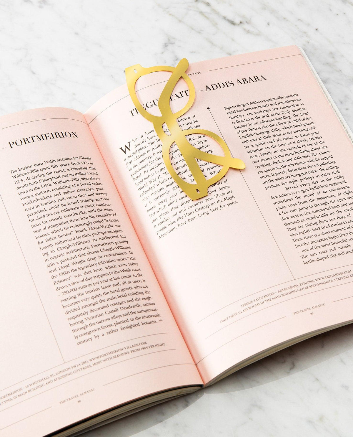 Open book with pink pages on marble, OCTAEVO Bookmark Riviera in gold brass across the center.