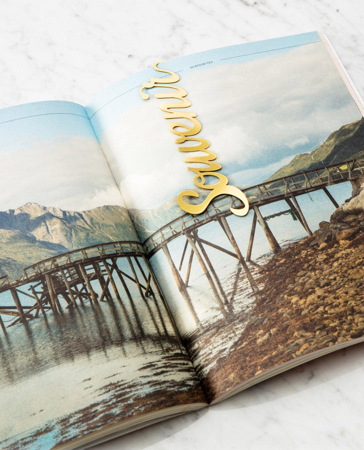 Open magazine with a scenic wooden pier photo; OCTAEVO Bookmark Souvenir in gold displayed across the page.