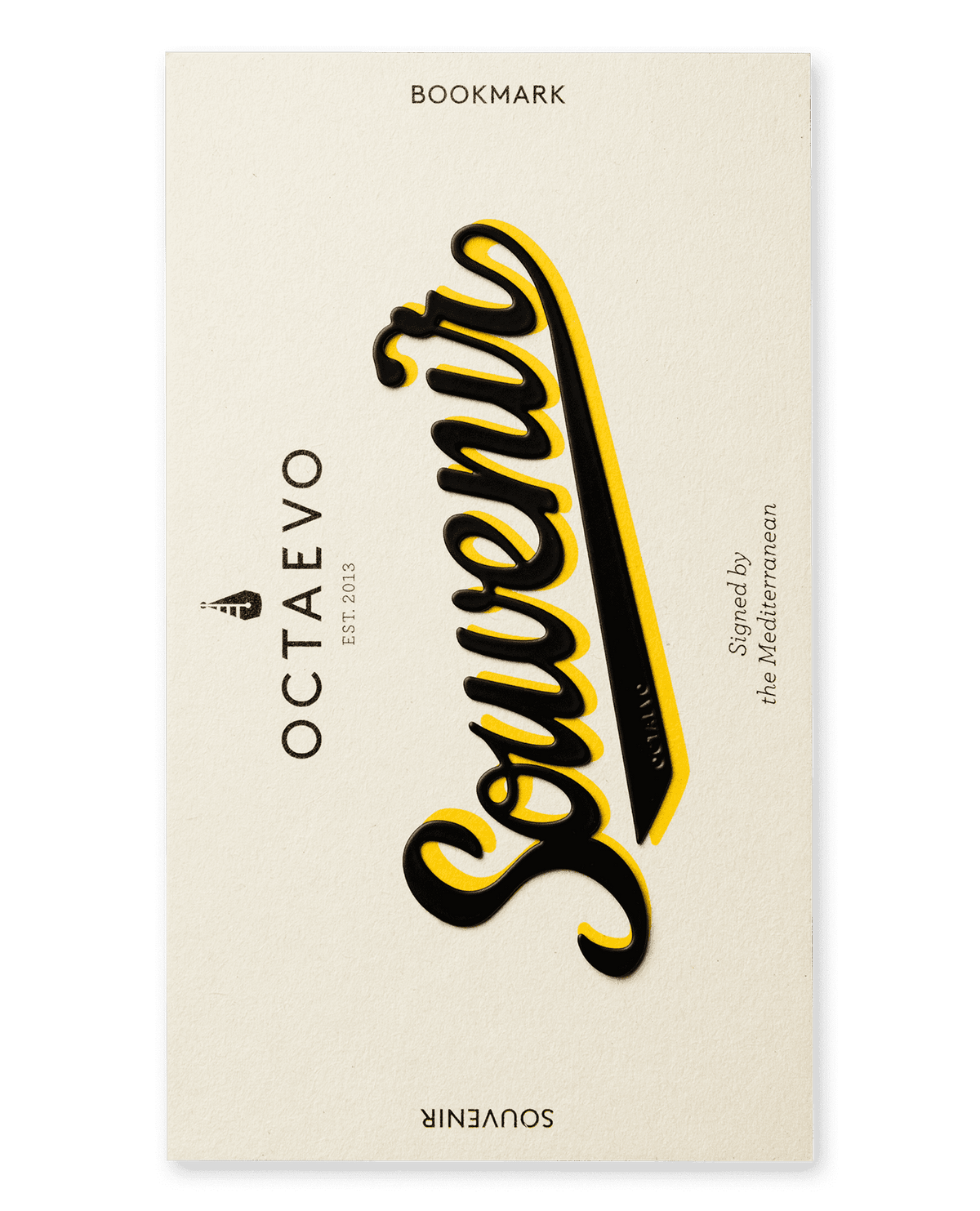 Cream-colored bookmark card with Souvenir in bold black script; OCTAEVO printed vertically on the left side.