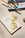 A paintbrush and palette beside OCTAEVO notebook The Voyage, featuring a gold sunglass bookmark on the cover.