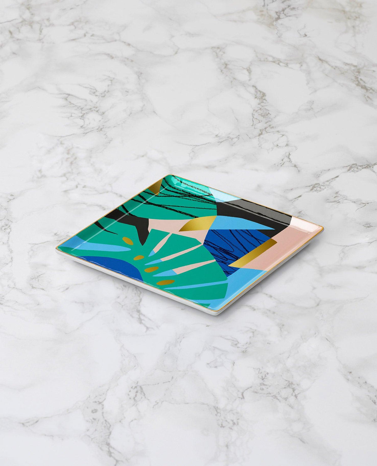 The Capri Ceramic Tray by OCTAEVO features a colorful abstract design and sits on a white marble surface.