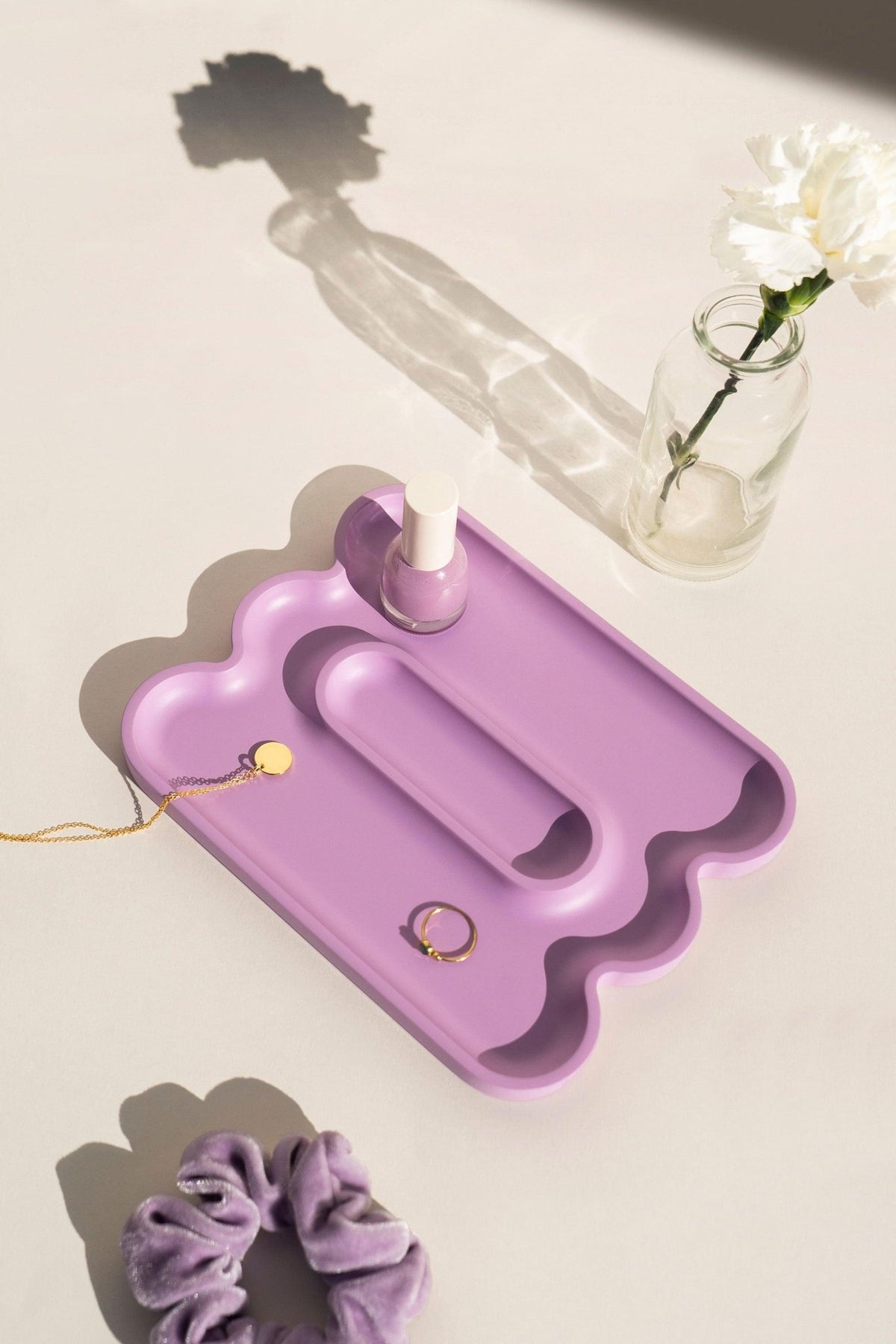The OCTAEVO Templo Wave Catchall in lilac holds nail polish, jewelry, and a scrunchie beside a white flower in a jar.