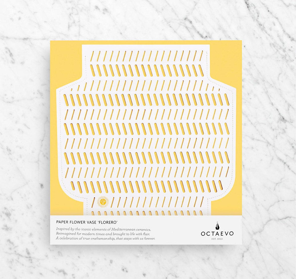 Flat-lay of the Coral Paper Vase by OCTAEVO, handcrafted from perforated white paper on yellow and marble background.