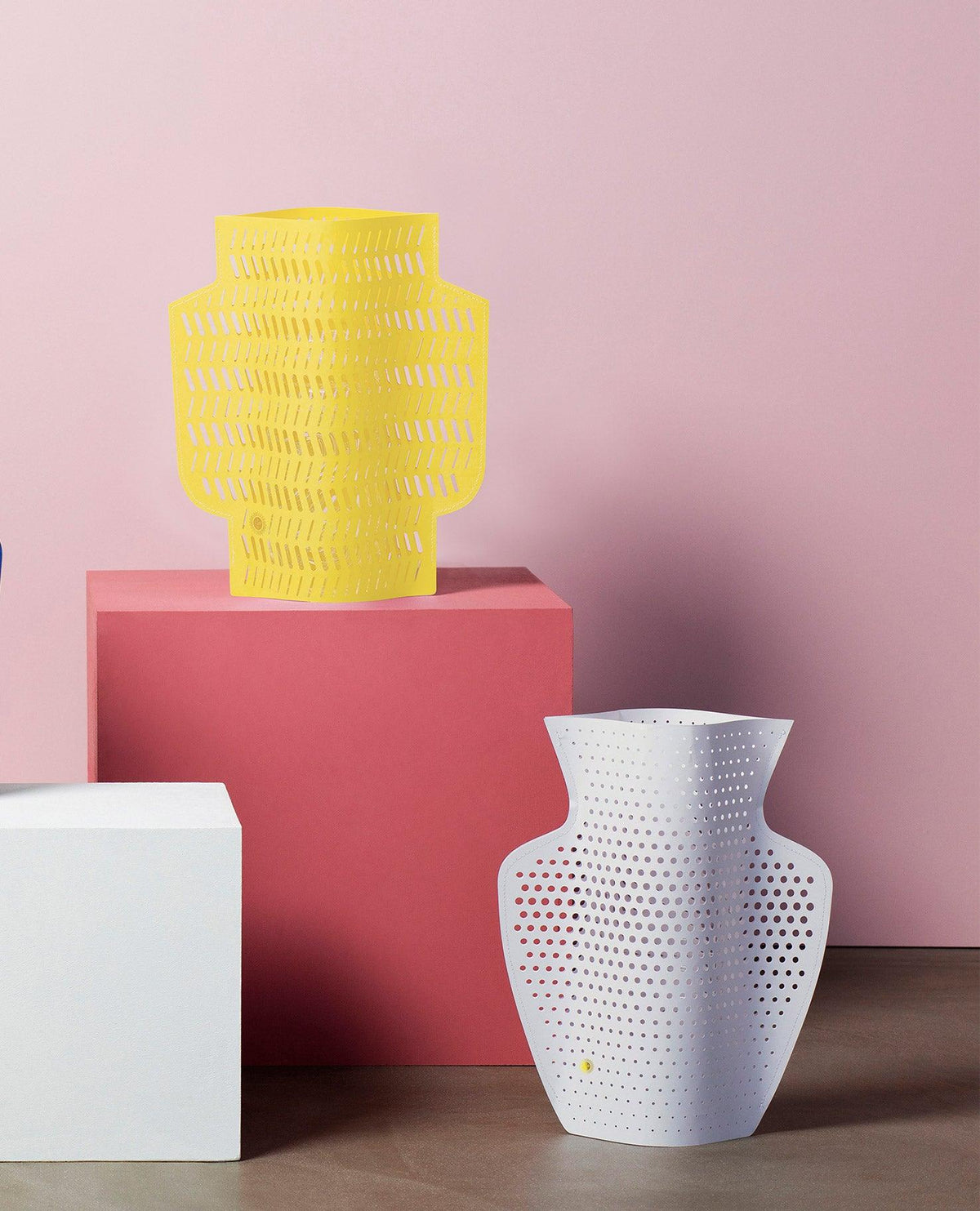 Two Dendra Paper Vases by OCTAEVO, in yellow and white, pop against a pink backdrop with geometric pedestals.