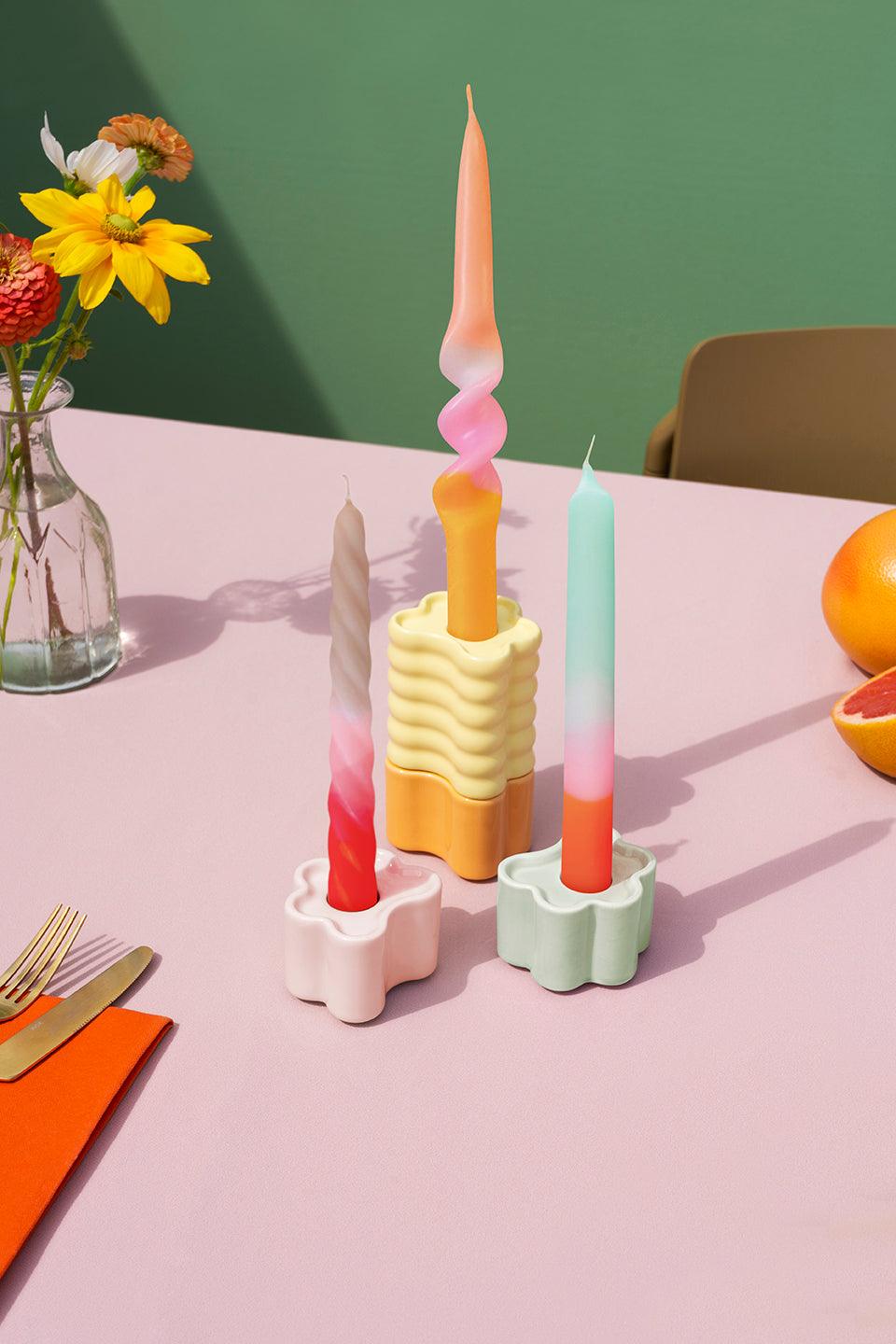 Three Octaevo Dip Dye Candles Sorbet in unique holders on a pink table, with flowers, fruit, and utensils nearby.