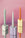 Three Flora Candle Holders by Octaevo with pastel candles are shown on a reflective surface against a pink background.