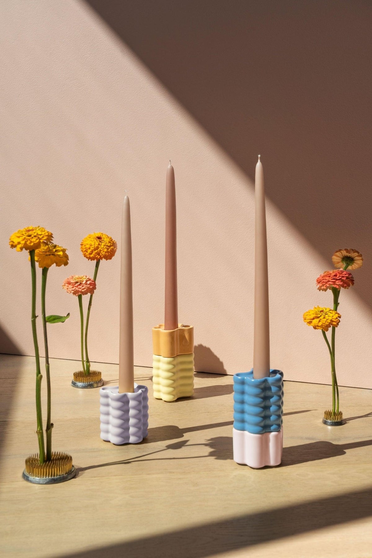 Three pastel ribbed flora holders with taper candles, surrounded by flowers in metal pin holders.