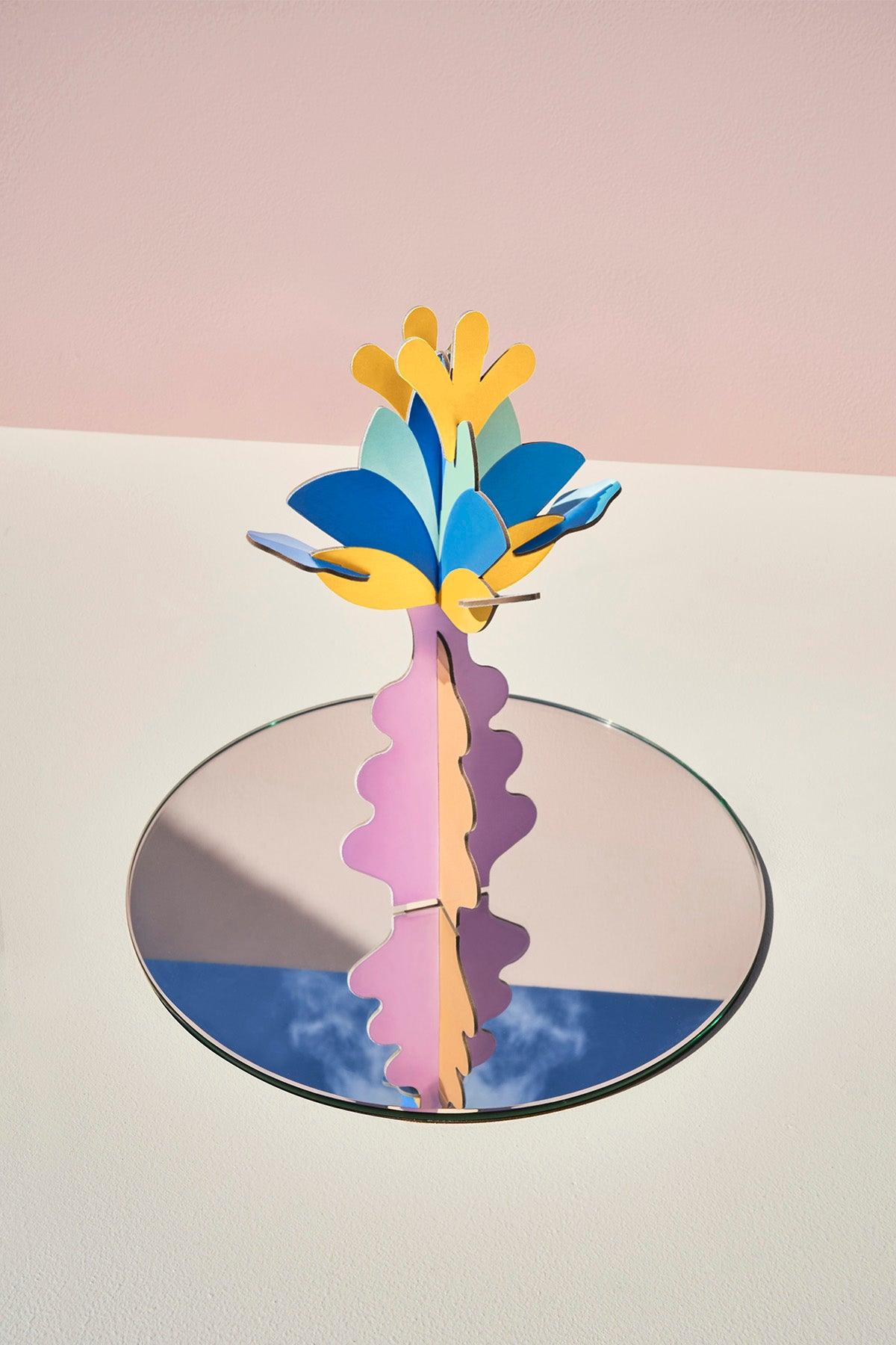 Arcadia Flower Paper Sculpture by OCTAEVO blooms on a mirror, echoing blue sky and clouds with a pink backdrop.